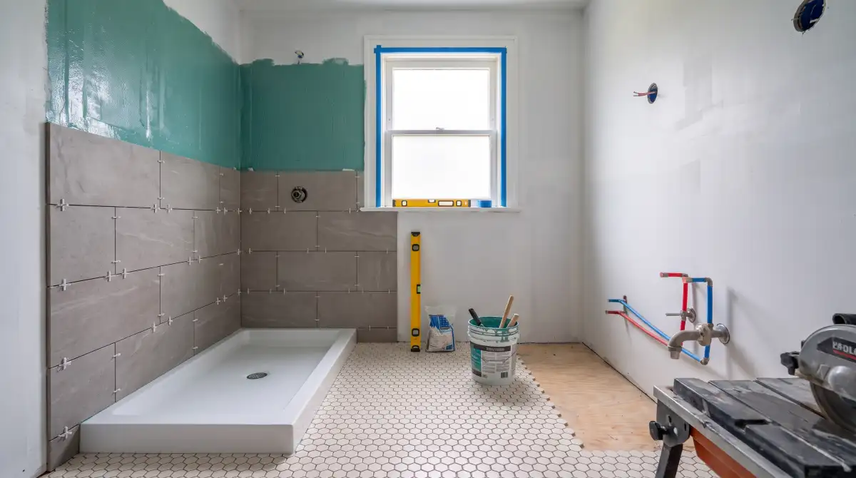 The same bathroom mid-tiling, large-format porcelain going up and hex floor going down